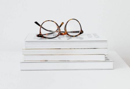 Image for "Want to Read our Publication?" Section. Photo of books stacked on top of one another with glasses sitting at top of stack.